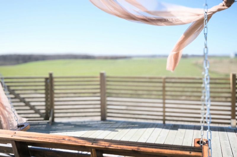 Wooden deck with a cozy porch swing and beautiful views of open green fields